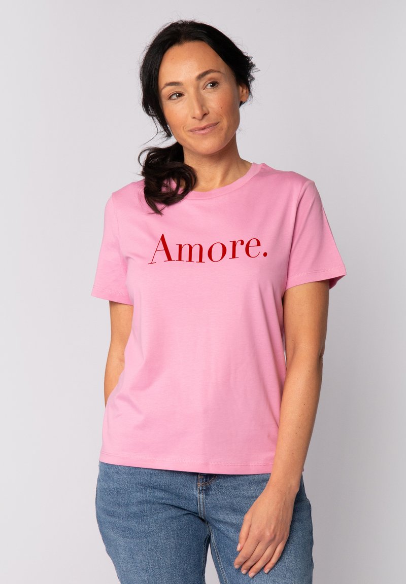 Roze katoenen t-shirt met een ronde hals en korte mouwen. Bevat het woord "Amore." gedrukt in vetrode letters op de borst.