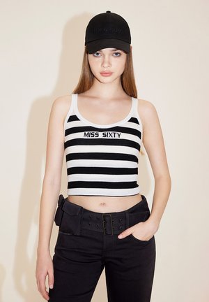 Sort og hvidstribet cropped top med "MISS SIXTY" broderet, parret med sorte bukser med bælte og en lomme til værktøj. Sort kasket.