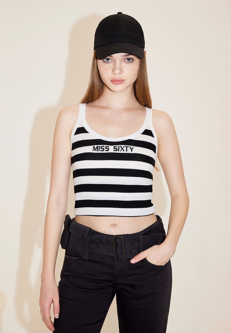 Sort og hvidstribet cropped top med "MISS SIXTY" broderet, parret med sorte bukser med bælte og en lomme til værktøj. Sort kasket.