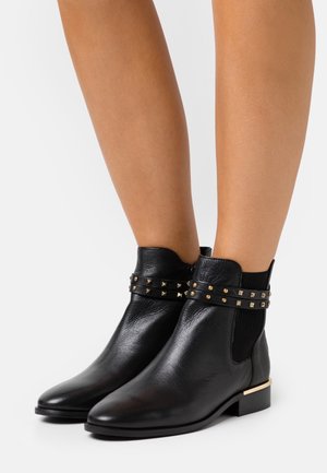 Stivaletti in pelle nera con dettagli di borchie dorate e pannelli elastici ai lati. Presentano un tacco basso a blocco e una texture liscia.