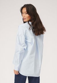 Lyseblå oversized button-up skjorte med lange ærmer, udstyret med en rygfold og manchetter, lavet af blødt bomuldsstof.