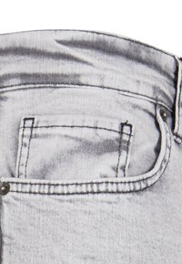 Jean en denim gris clair avec une poche arrière visible, des rivets en métal et des coutures piquées. Le tissu a une texture légèrement usée.