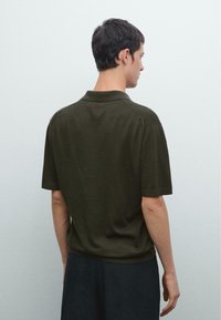 Polo shirt verde oliva a maniche corte con colletto classico, caratterizzato da una texture morbida e polsini a coste. Design semplice ed essenziale.