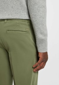 Gray sweater with ribbed cuffs paired with green, tailored trousers featuring a back pocket and subtle logo detail. Smooth fabric texture.