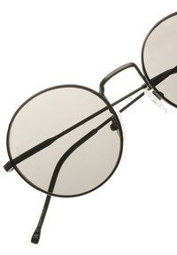 Pyöreät mustat aurinkolasit tummennetuilla linsseillä, joissa on ohut metallikehys, nenätyynyt ja hoikat sangat. Linssit ovat hieman heijastavat.