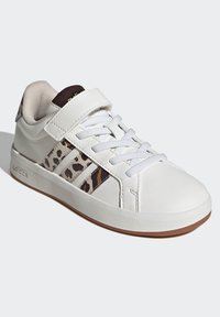 White sports shoes featuring a Velcro strap, textured leather upper, brown leopard print accents, and gray laces. Rubber sole with slight curvature.