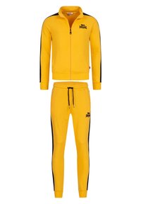 Žltý športový komplet pozostávajúci z bundy na zips s čiernymi bočnými pruhmi a joggingových nohavíc s elastickým pásom a logom.