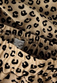 Tissu en imprimé léopard doré avec des taches noires. Texture lisse avec une finition brillante. Détail de bande élastique visible sur les bords.