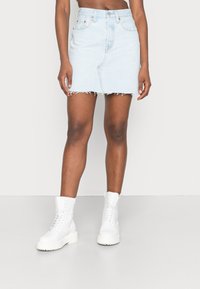 Ljusblå denim miniskirt med fransad fåll, femfickdesign och framtill dragkedja. Matchad med vita ankelstövlar.