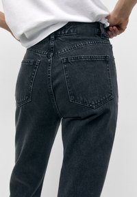 Mustat farkut, joissa on jämäkkä muotoilu, sisältäen kaksi takataskua ja merkin vyötärönauhassa. Kankaan pinta on klassinen ja teksturoitu.