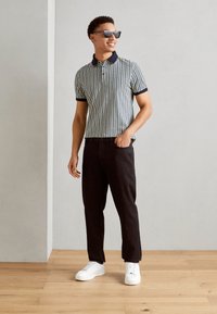 Polo à manches courtes avec un col marine et un motif en bleu clair et blanc. Porté avec un jean sombre et des baskets blanches.