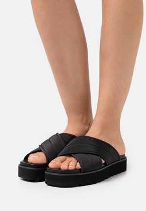 Svarta flip-flops med vadderade korsremmar och en tjock, texturerad sula. Har en upphöjd plattform för ökad komfort.