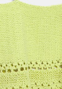 Tissu tricoté vert clair avec des motifs de points texturés et des détails décoratifs en dentelle ajourée.