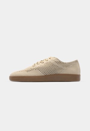 Beige perforated sneaker with round toe, lace-up design, textured fabric upper, and brown rubber sole. Features small ventilation holes throughout.