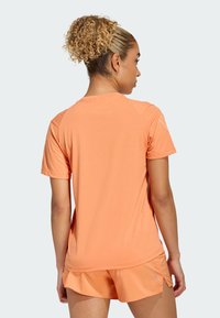 Lys oransje trenings-T-skjorte med korte ermer, glatt tekstur, rund hals og sidesplitter, brukt sammen med matchende shorts.