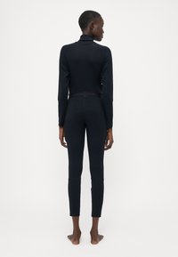 Haut noir à manches longues avec col montant, design sans couture, et leggings ajustés avec une taille marquée, vus de dos.