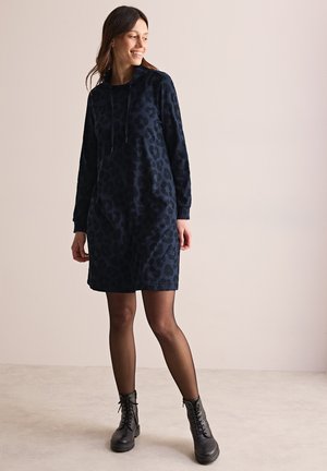 Robe à capuche bleu marine avec imprimé léopard, manches longues, poche avant et capuche avec cordon de serrage. Modèle associé à des bottes de combat noires.