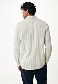 Pruhovaná košile na knoflíky ve svetle zelené a bílé barvě. Obsahuje límec, dlouhé rukávy a zakřivený spodní lem. Měkká tkanina s texturovaným povrchem.