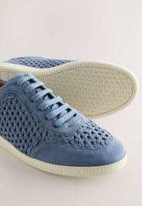 Sneakers in camoscio azzurro chiaro con pannelli laterali intrecciati, lacci piatti e suola in gomma bianca testurizzata. Punta liscia e dettagli imbottiti nel design.