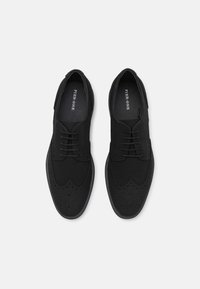 Schwarze Lederschuhe mit Wingtips-Design, perforierten Akzenten und einer abgerundeten Zehenpartie. Schnürsenkel und dezente Markenkennzeichnung sind im Inneren sichtbar.