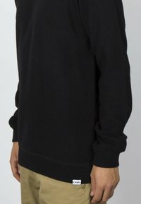 Schwarzes Sweatshirt aus weichem Stoff mit langen Ärmeln, gerippten Bündchen und einem sichtbaren Clepto-Label am Saum.