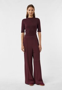 Mauve Oberteil mit kurzen Ärmeln, kombiniert mit weiten mauvefarbenen Hosen. Beide Teile haben eine glatte Textur und klare Linien. Legere Schuhe sind ebenfalls enthalten.