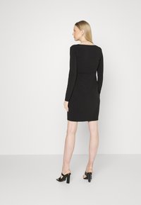 Vestido preto de mangas longas com silhueta justa, decote redondo e textura suave. Combinado com sandálias de salto pretas.