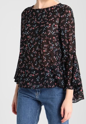 Musta kukkakuvioinen pusero, jossa on läpikuultava kangas, pyöreä pääntie ja kellohihat, joissa vaaleanpunaisia ja sinisiä kukkakuoseja. Yhdistetty sinisiin farkkuihin.