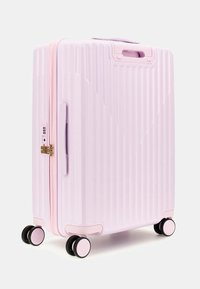 Valigia rigida di colore rosa chiaro con scanalature verticali, zipper dorato, doppio manico laterale e quattro ruote nere per una facile manovrabilità.