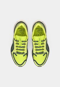 Neon gule atletiske sko med mesh materiale og sorte accenter. Har flade snørebånd, en tekstureret sål og forstærket tåhætte.