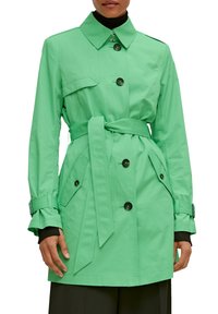 Trench-coat vert clair avec une taille ceinturée, fermeture à boutons à l'avant et deux poches latérales. Comprend un col et des sangles d'ajustement aux poignets.