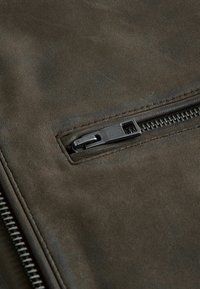 Dunkelolivgrüner Lederstoff mit structuriertem Oberflächen und einer Reißverschlusstasche mit schwarzem Metallzubehör.