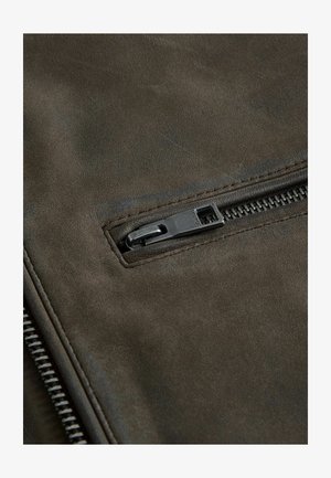 Tummanoliivinvihreä nahkakangas, jossa on teksturoitu pinta ja vetoketjullinen tasku mustalla metallivarustuksella.