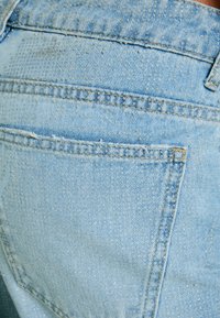 Light blue denim jeans with a textured surface, featuring a back pocket, visible stitching, and a slight distressed look.
