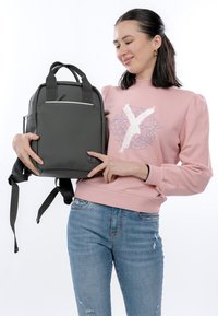 Harmaa reppu, jossa on sileä pinta, suorakulmainen muoto, yläkahvat, säädettävät olkahihnat ja etutaskussa vetoketju.