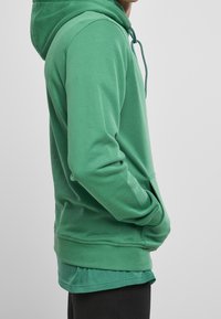 Grüner Kapuzenpullover mit lockerem Schnitt, gerippten Bündchen und Saum. Hergestellt aus weichem Stoff, mit einer Fronttasche und verstellbarer Kapuze mit Kordelzug.