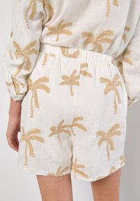 Vita shorts med ett texturerat mönster av palmer i beige, med elastisk midja och avslappnad passform. Mjuk tygkvalitet, avslappnad design.