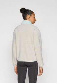 Ανοιχτό γκρι φλις πουλόβερ με γιακά μέντας. Διαθέτει χαλαρή εφαρμογή και μακριά μανίκια. Φορεμένο με μαύρο εφαρμοστό κολάν.