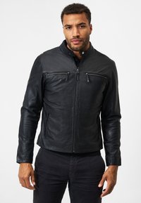 Zwarte leren jas met een rits aan de voorkant, staande kraag en twee ritszakken op de borst. Gladde textuur, slim fit ontwerp en subtiele glans.