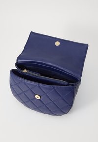 Geantă din piele matlasată de culoare bleu marin, cu un închizător aurit. Interiorul dispune de un buzunar cu fermoar și un compartiment deschis pentru stocare.
