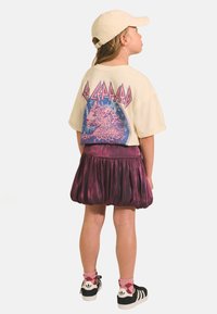 T-shirt crème à manches courtes avec un graphique de léopard coloré, associé à une jupe plissée violette brillante et des baskets noires avec des chaussettes roses.