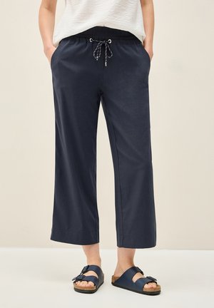 Navy wide-leg pants with an elastic waistband and drawstring, featuring side pockets. Smooth texture, paired with dark blue slide sandals.