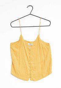 Gul ärmlös blus med tunna band och framknäppning täckt av tyg, hängande på en svart klädhängare mot en vit bakgrund.