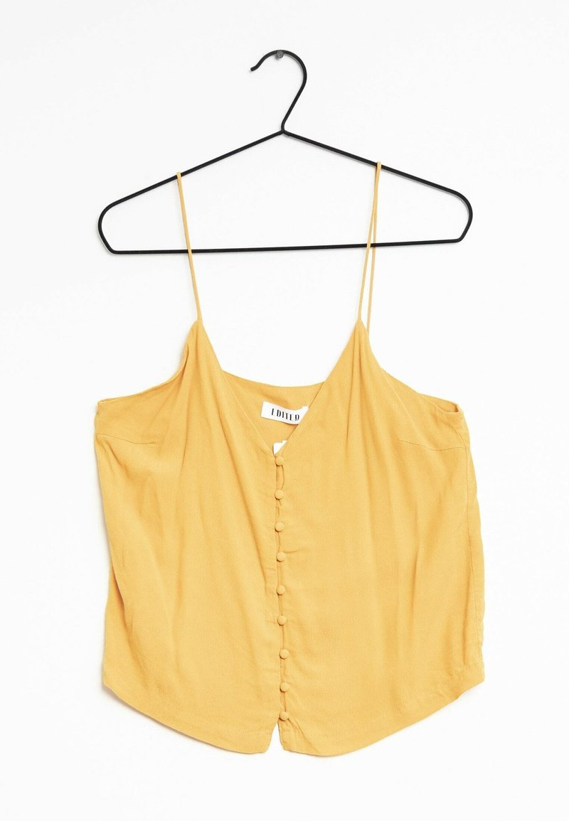 Gul ärmlös blus med tunna band och framknäppning täckt av tyg, hängande på en svart klädhängare mot en vit bakgrund.