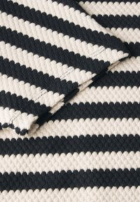 Textil med svarta och off-white zickzackränder. Tyget har en vävd struktur och synlig sömnad längs kanterna.