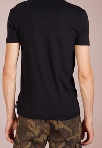 Svart bomulls t-shirt med kort ärm, figurnära design och en etikett på sidan, tillsammans med kamouflagebyxor. Texturerat tyg.