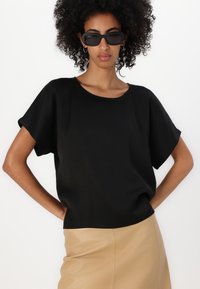 Top nero a maniche corte realizzato in tessuto liscio, con scollatura rotonda. Abbinato a una gonna in pelle beige per creare contrasto.