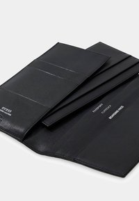 Zwarte leren reisebestuurder met gelabelde vakken voor paspoort, valuta en instapkaart, voorzien van een omslagklep en gestikte randen.