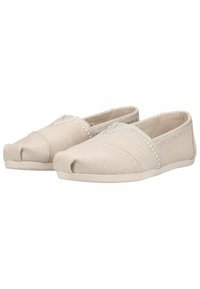 Chaussures beige en toile à enfiler avec des détails cousus et des semelles en caoutchouc profilées basses, vues côte à côte sur un fond blanc.