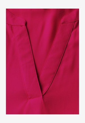 Fuchsiová halenka se švem ve tvaru hlubokého V, vyznačující se jemnými švy a hladkou, lehkou texturou.